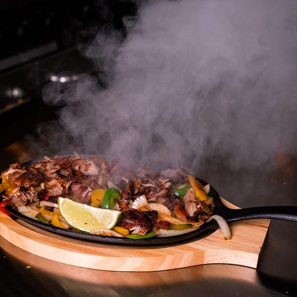 Sizzling fajitas with chicken, peppers, onions, and a lime wedge on a cast iron skillet.